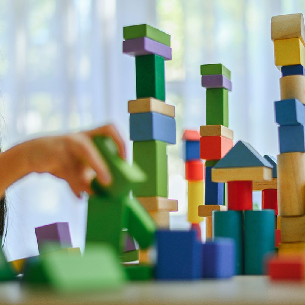 Little Girl In A Colorful Shirt Playing With Construction Toy Bl