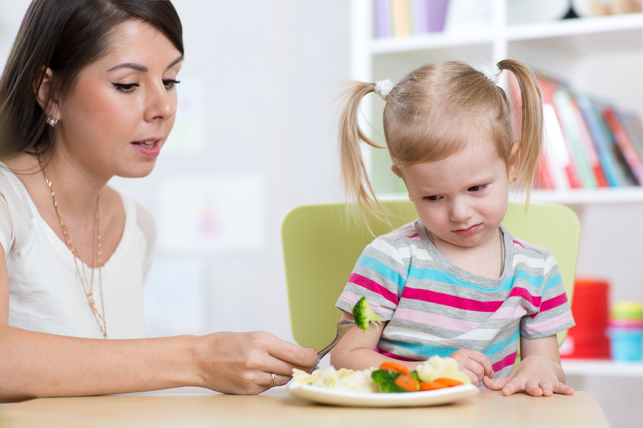 Child Girl Looks With Disgust At Healthy Vegetables. Mother Conv