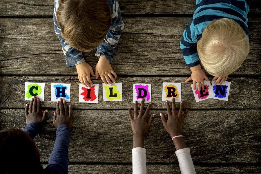 Top View Of Four Children Of Mixed Races Touching A Word Childre